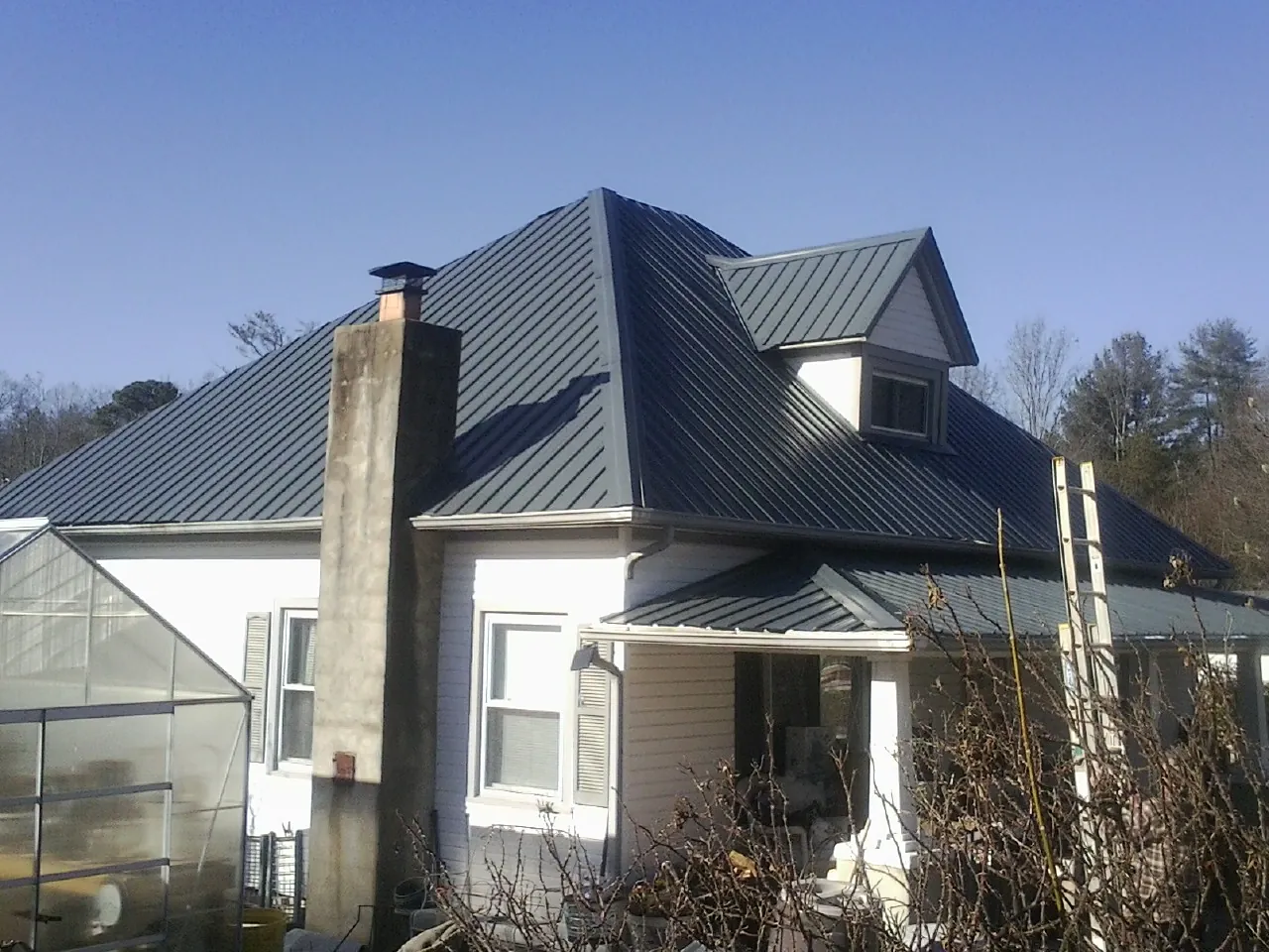 Dark blue standing seam metal roof on a white farmhouse with dormer — Slate & Tile Roof Repair by Roofing Brothers in Osceola