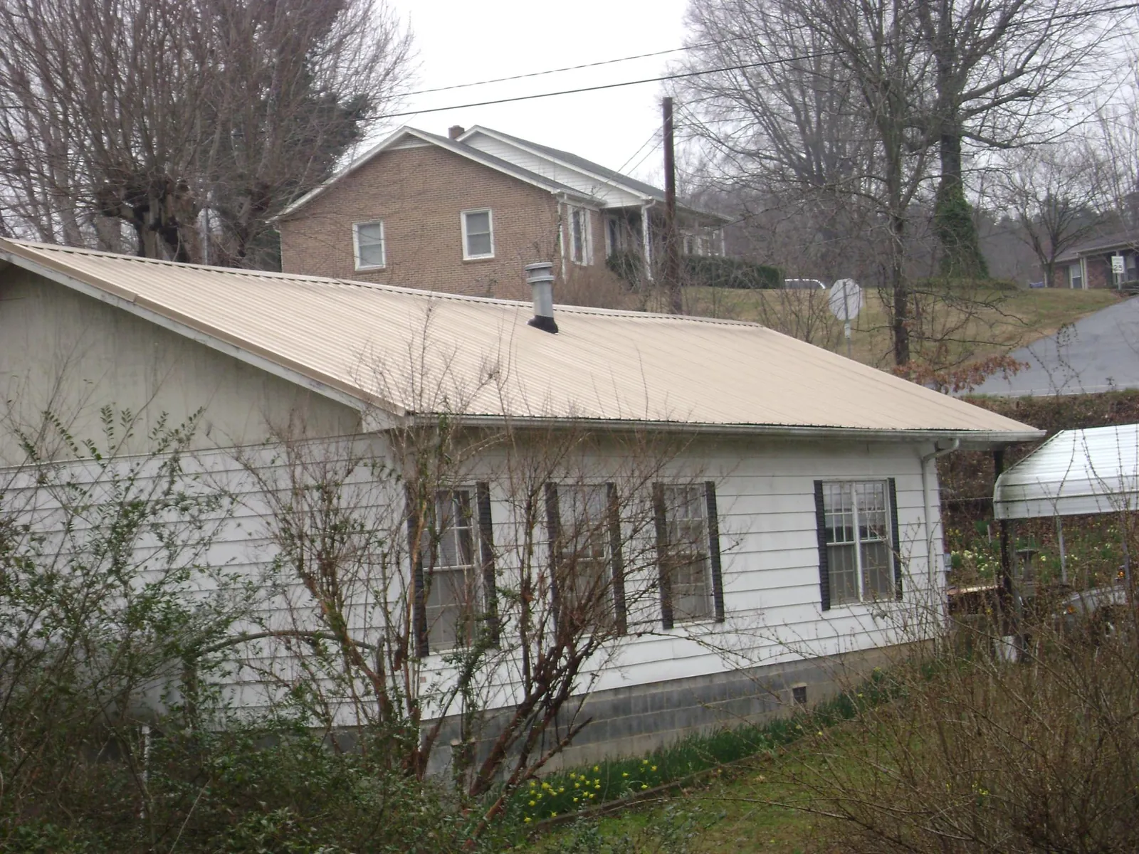 Tan metal roof on a white sided house set into a hillside — Commercial Roofing by Roofing Brothers in Osceola